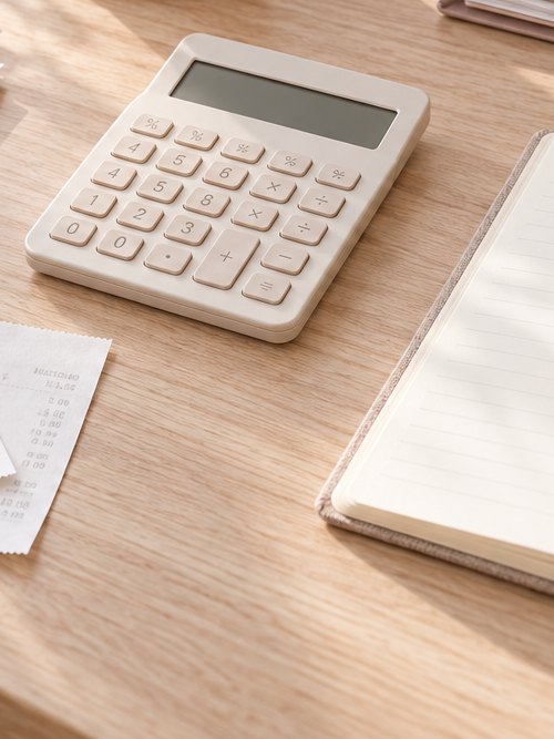 A calculator, receipts and notebook on an oak desk